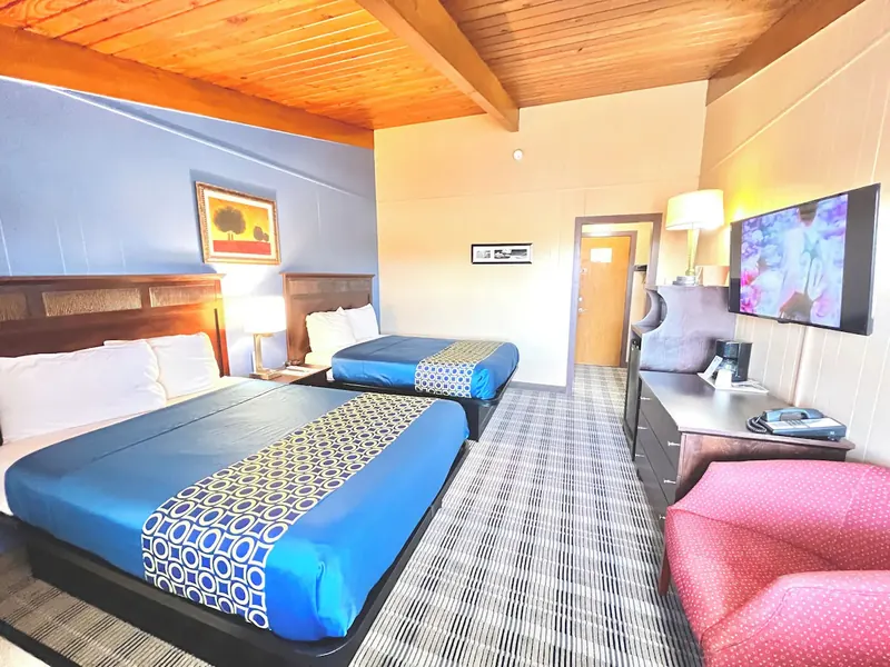 Room with two queen beds, a pitched timber ceiling and a red armchair